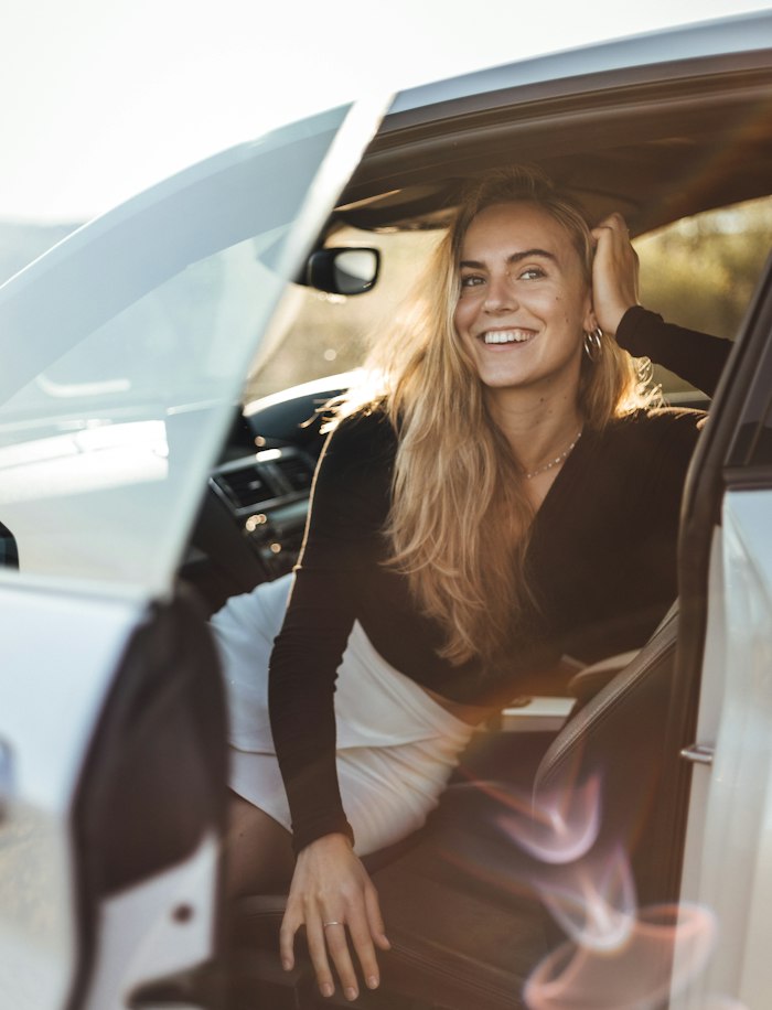 Jeune conductrice souriante au volant, portière ouverte