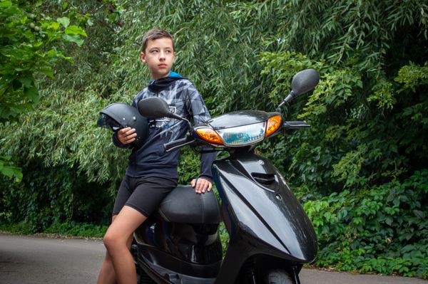 Adolescent sur un scooter 50 cm³, casque à la main